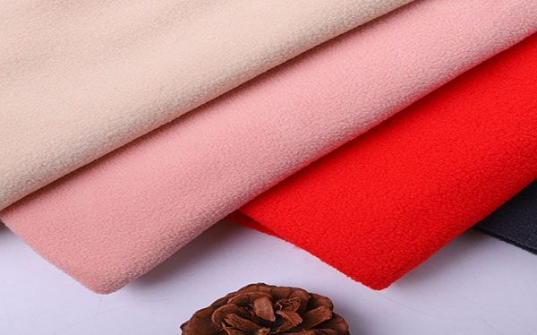 Fleece fabric is a soft, light and warm textile material. It is generally preferred in clothing used in cold weather conditions.

The properties and production process of polar fabric are as follows:

### Properties of Fleece Fabric
- **Material:** Generally produced from polyester. This material is preferred because it is durable and lightweight.
- **Thermal Insulation:** Polar fabric provides good thermal insulation thanks to its fiber structure. This helps it maintain body heat in cold weather conditions.
- **Repelling Moisture:** Polyester fibers do not absorb moisture, so fleece fabric dries quickly and removes moisture from the body.
- **Lightness:** It offers comfortable use with its soft and light structure.
- **Breathability:** Fleece fabric is breathable, which provides comfort by reducing sweating.
- **Durability:** It is resistant to wear and can be used for a long time.

### Fleece Fabric Production
1. **Raw Material Preparation:**
 - Polyester fibers are obtained from recycled plastic bottles or petrochemical raw materials.

2. **Yarn Production:**
 - Polyester fibers are turned into thread.

3. **Knitting Process:**
 - Threads are turned into fabric in large knitting machines. At this stage, the texture of the fabric is determined.

4. **Feathering:**
 - Knitted fabric is processed in fluffing machines. This process makes the fibers on the surface of the fabric become fluffy and soft.

5. **Heat Treatment:**
 - The fabric is processed at a certain temperature to ensure that the fibers are fixed. This helps the fabric maintain its shape and structure.

6. **Painting and Finishing:**
 - The fabric is dyed in the desired color and treated with softeners. This process increases the softness of the fabric and makes its color permanent.

7. **Cutting and Sewing:**
 - The finished fleece fabric is cut and sewn for use in garment production.

### Usage Areas of Polar Fabric
- **Outerwear:** Coats, jackets, vests.
- **Underwear:** Underwear, pajamas.
- **Accessories:** Hat, gloves, scarf.
- **Home Textile:** Blanket, bedspread.
- **Sports Wear:** Trekking, camping, ski clothes.

Polar fabric has a wide range of uses thanks to its high thermal insulation, lightness and durability properties and is especially ideal for outdoor activities.